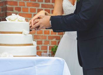 Midsection of newlywed couple cutting wedding cake in ceremony