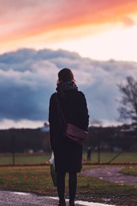 Rear view of woman standing on landscape against sky during sunset