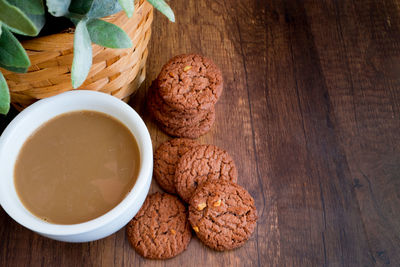 A cup of coffee and cookies on wooden table abd black background