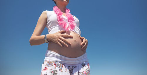 Midsection of pregnant woman with touching belly against clear sky