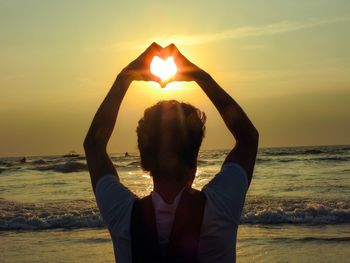 Young man at beach against sky during sunset