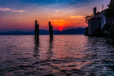 Silhouette wooden posts in sea against sky during sunset