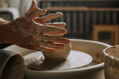 Close-up shot of ceramic cup spinning on potters's wheel and hands molding clay