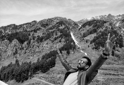 Young man with arms raised standing on mountain against sky