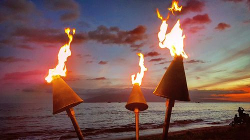 Lit candles on beach against sky during sunset