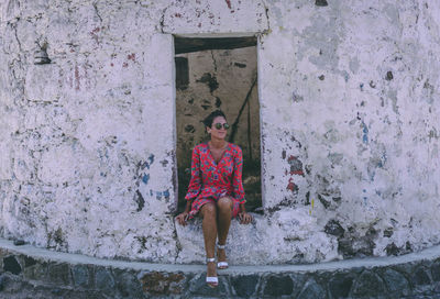 Woman sitting against weathered wall