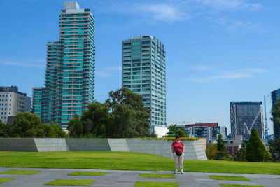 Rear view of man standing by modern buildings against sky