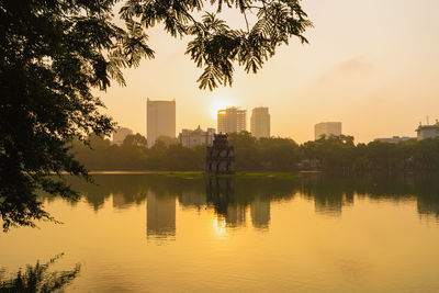 Lake and buildings against sky during sunset