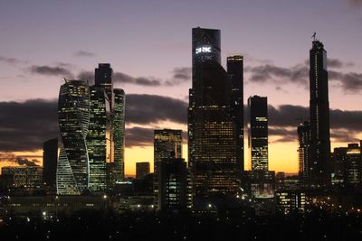 Illuminated buildings in city against sky at dusk