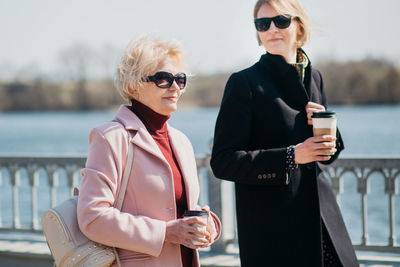 Woman wearing sunglasses holding coffee while standing outdoors