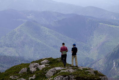 Rear view of men standing on mountain against sky