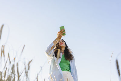 Happy woman using smart phone in field under clear sky