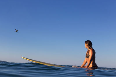 Woman surfing in sea against blue sky