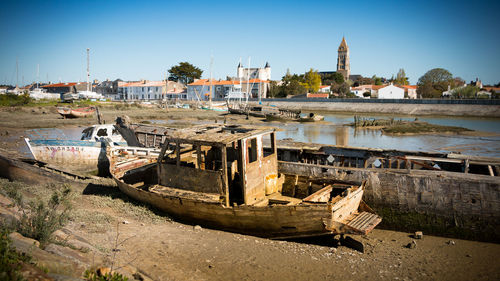 Abandoned boats in river by buildings against clear sky