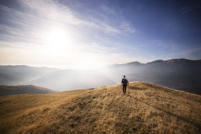 Rear view of male backpacker walking on mountain against sky