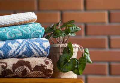 Stack of clean bath towels and greennery on wooden table near red brick wall. space for text