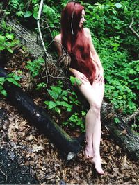 Naked young woman leaning on fallen tree at forest