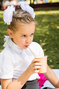 Cute little schoolgirl drinks apple juice from an eco cup with a straw at a picnic in the park
