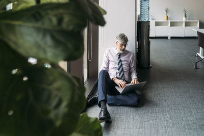 Businessman using laptop sitting on floor in office