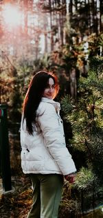 Young woman looking away while standing against trees
