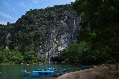 Boats moored on sea by cliff against sky