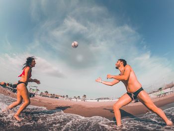 Low angle view of friends playing on beach against sky