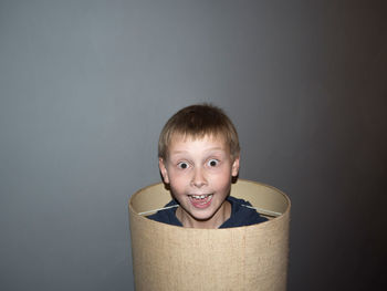 Portrait of surprised boy in cylindrical shape cardboard against wall