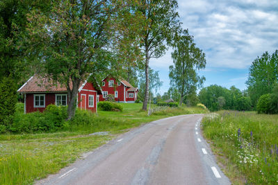 Road passing a red cottage with white corners in summer time