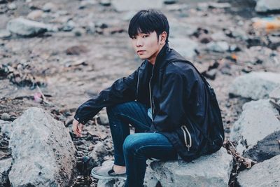 Side view of young man sitting on rock