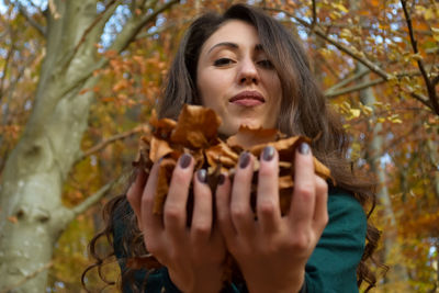 Portrait of young woman holding autumn leaves standing outdoors
