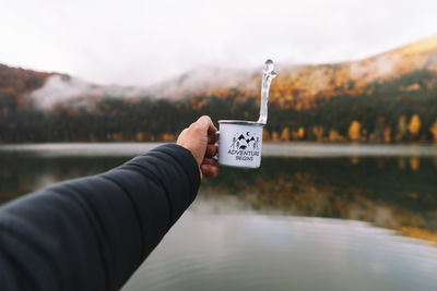 Young traveler male holding a mug with water in the wilderness forest,autumn season. 