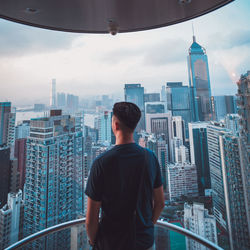 Rear view of man looking at cityscape against sky