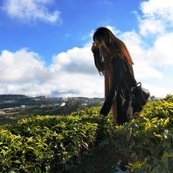 Side view of woman standing amidst plants on field against sky