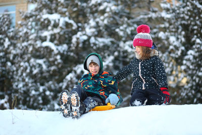 Winter portrait of children with a plastic sled sliding on a snowy slope and making a snowman