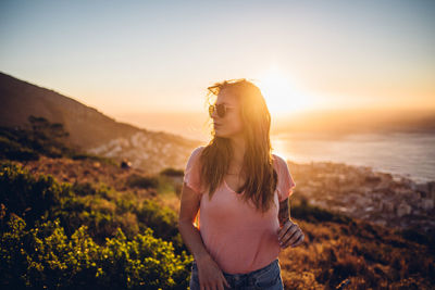 Beautiful woman standing on land against sky during sunset