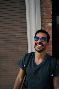 Portrait of young man wearing sunglasses standing against brick wall