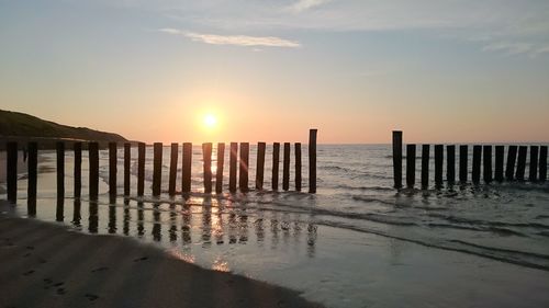 Wooden posts on beach against sky during sunset