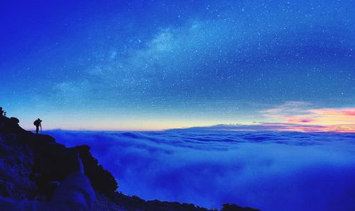 Silhouette hiker on mountain by cloudscape against sky at night