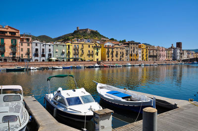 Boats moored in canal by buildings against clear blue sky