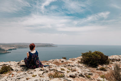 Rear view of woman sitting on cliff against sea