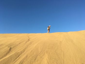 Low angle view of mature man standing at desert against clear blue sky
