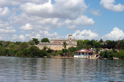 View of building by river against cloudy sky