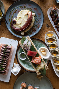 Assortment of gourmet japanese dishes on a wooden table, including sashimi, octopus, and gyoza