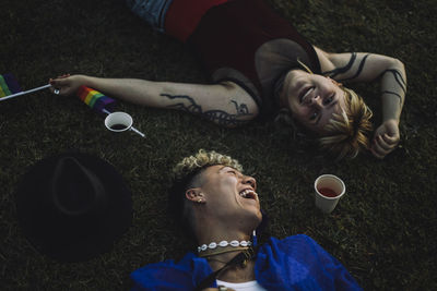 Cheerful young man lying by non-binary friend on grass at park during sunset