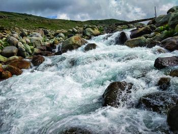 Stream flowing through rocks in sea against sky