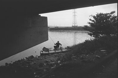 Man sitting on bridge over river against sky