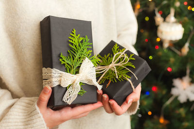 Woman holding small gifts in her hands. close up. decorated christmas tree on background