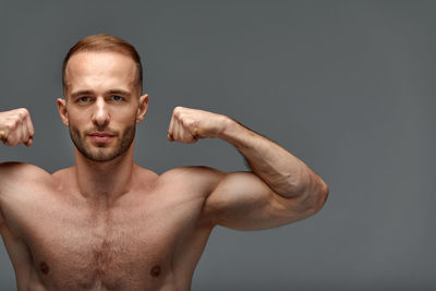 Shirtless man with arms raised against black background