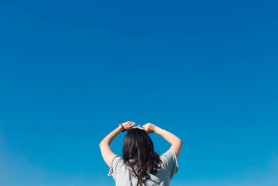 Low angle view of woman against clear blue sky