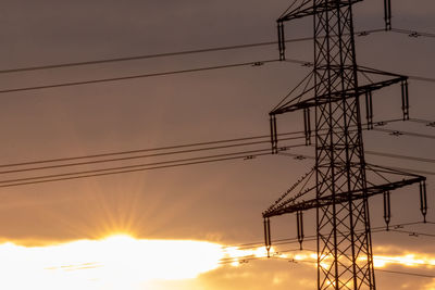 Low angle view of electricity pylon against sky during sunset